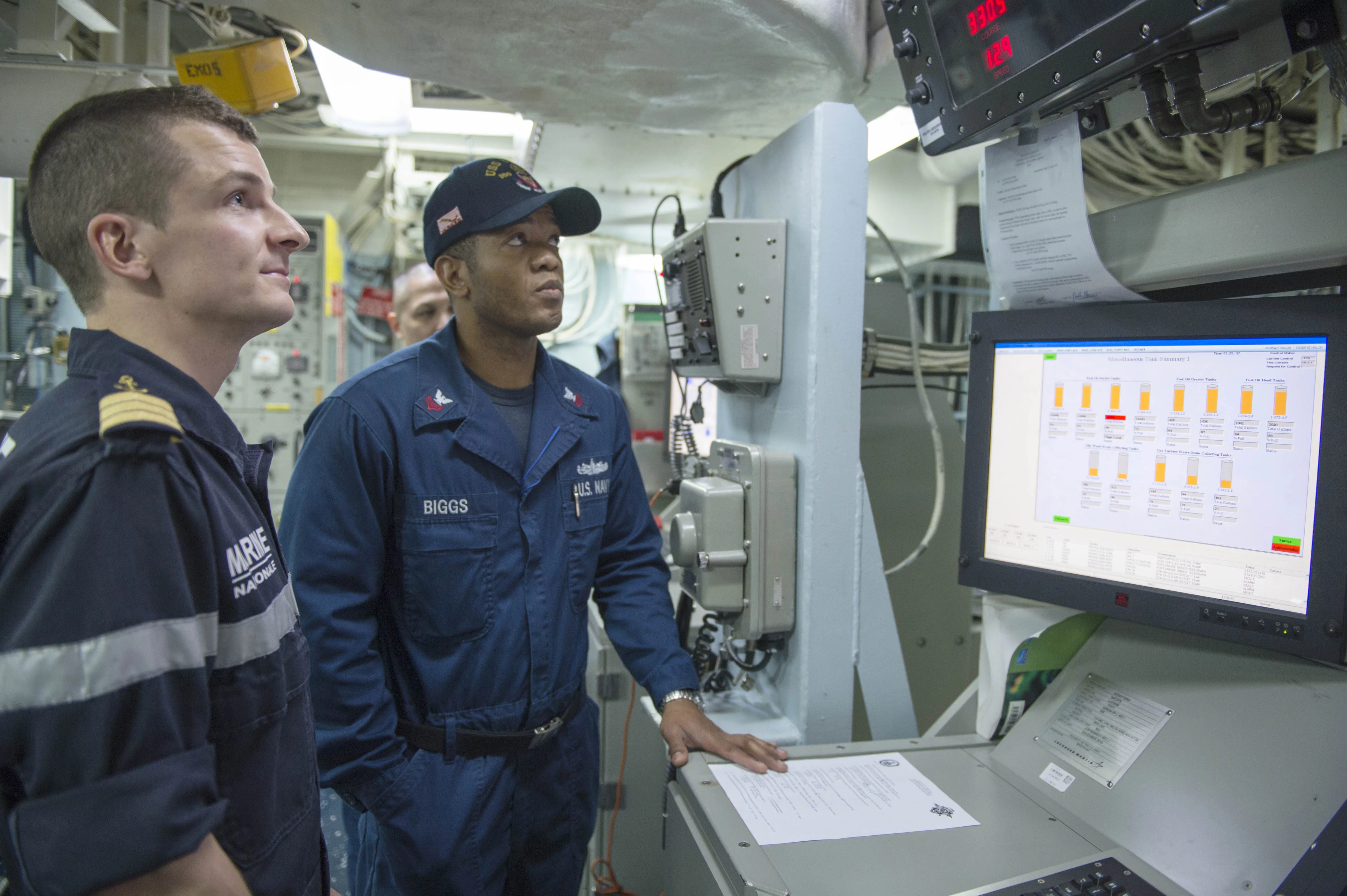 Un marin américain présente à un marin français la console de contrôle central du destroyer