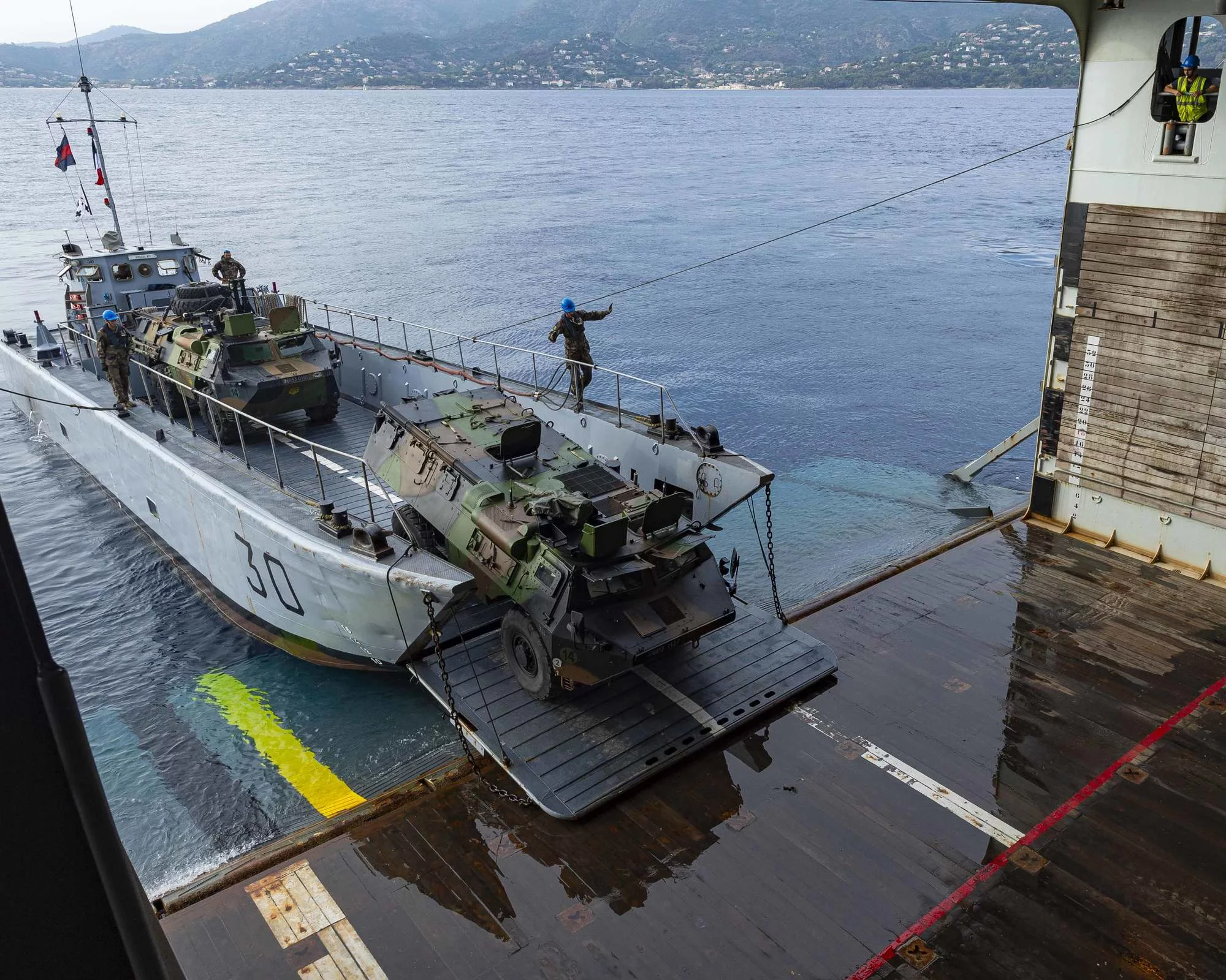 Des véhicules de l'armée de terre embarquent sur un chaland de transport de matériel (CTM)