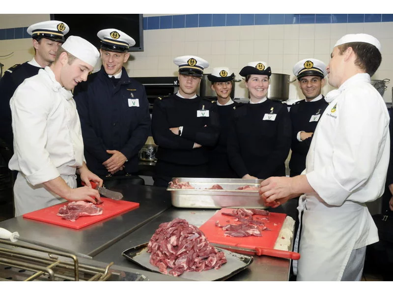 Des cuisiniers de la Royal Navy travaillent sous les yeux d'élèves commissaires de la marine nationale